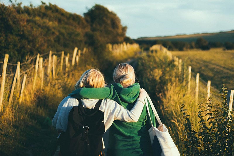 Back view of two friends walking through a field